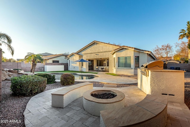 back of property featuring exterior kitchen, a fenced in pool, a patio area, and a fire pit