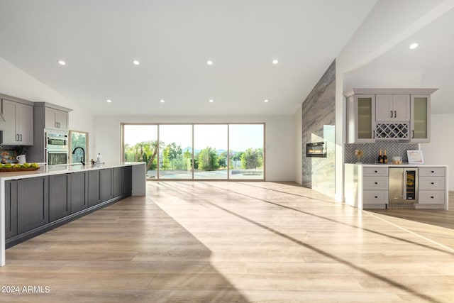 kitchen featuring gray cabinetry, sink, beverage cooler, backsplash, and light wood-type flooring