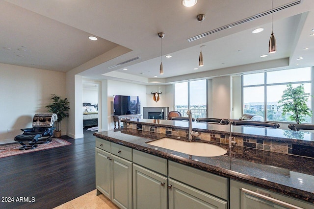 kitchen featuring dark stone countertops, hardwood / wood-style flooring, a tray ceiling, and sink