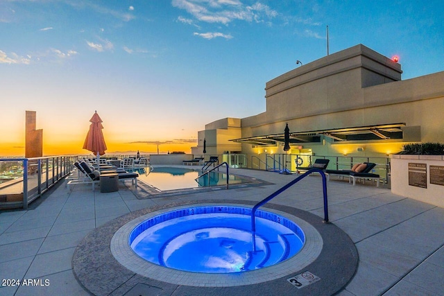 pool at dusk with a patio and a hot tub