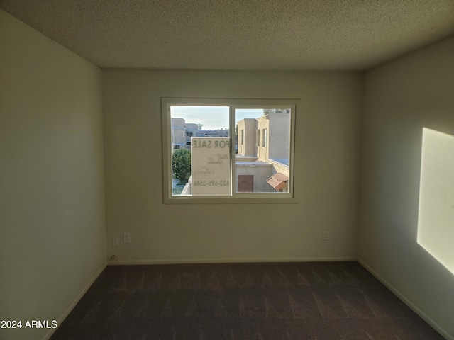 spare room featuring dark carpet, a textured ceiling, and baseboards