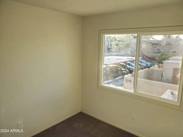 empty room with a textured ceiling, dark carpet, and baseboards