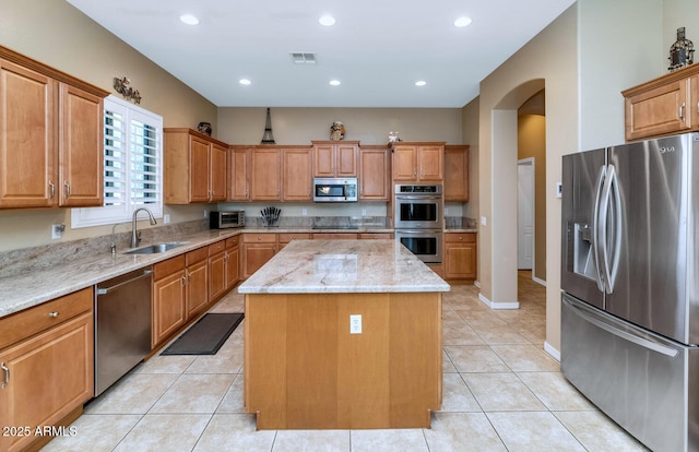 6133 W Fetlock Ter, Phoenix, AZ 85083 - kitchen with stainless steel appliances, a sink, a center island, arched walkways, and light stone counters