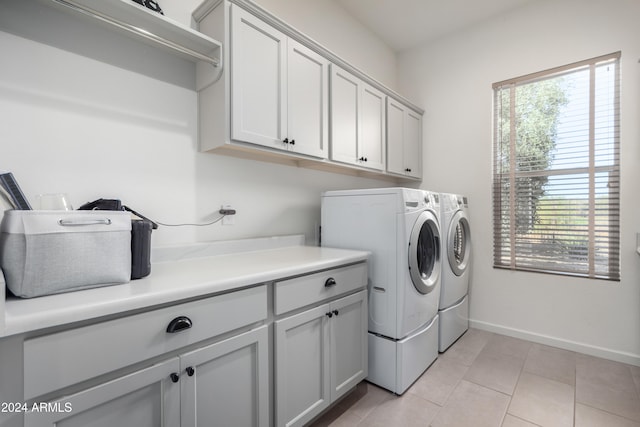 laundry area with a wealth of natural light, washer and clothes dryer, light tile patterned flooring, and cabinets