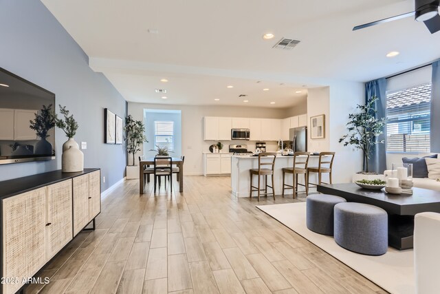 living area featuring visible vents, light wood-style floors, and a healthy amount of sunlight