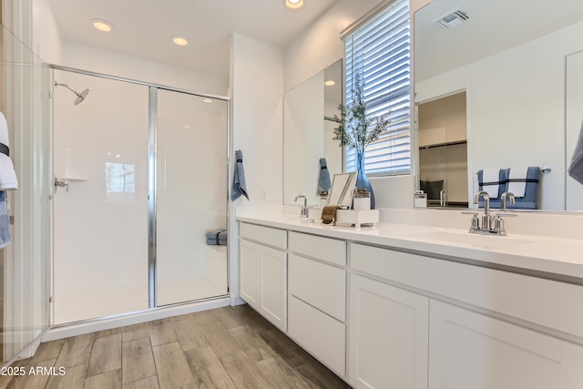 full bath featuring wood finished floors, a sink, a stall shower, double vanity, and visible vents