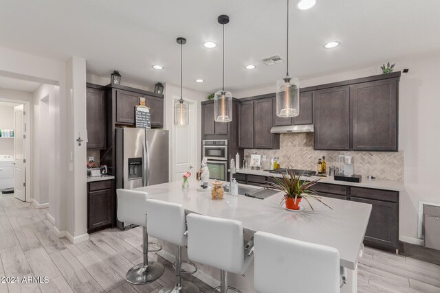 kitchen featuring pendant lighting, light hardwood / wood-style flooring, an island with sink, appliances with stainless steel finishes, and dark brown cabinets