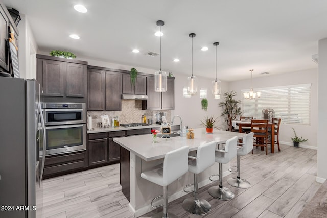 kitchen featuring dark brown cabinetry, hanging light fixtures, stainless steel appliances, a kitchen island with sink, and a breakfast bar