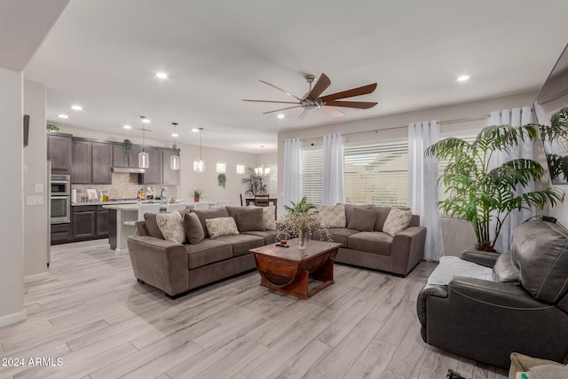 living room with ceiling fan with notable chandelier and light hardwood / wood-style floors