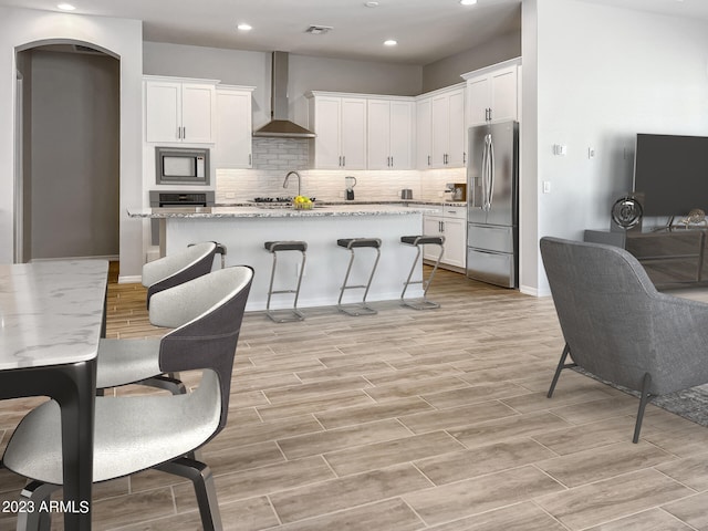 kitchen with light stone counters, white cabinets, light hardwood / wood-style flooring, wall chimney range hood, and stainless steel appliances