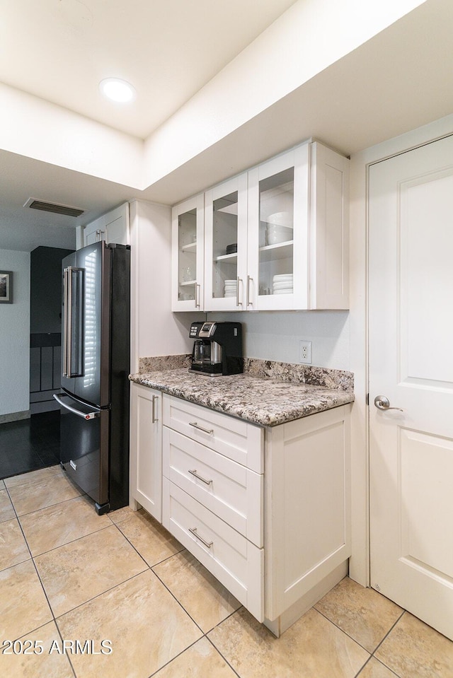 kitchen with white cabinets, light stone counters, glass insert cabinets, and freestanding refrigerator