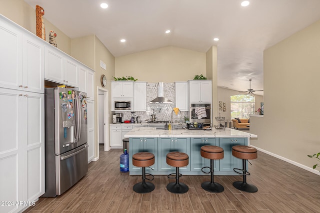 kitchen with wall chimney range hood, dark wood-type flooring, an island with sink, white cabinetry, and appliances with stainless steel finishes