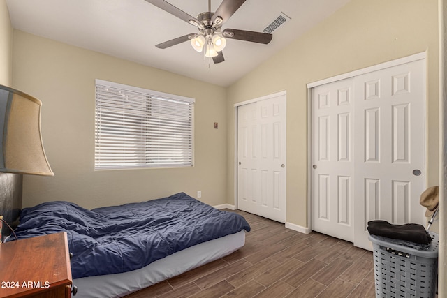 bedroom with ceiling fan, multiple closets, dark hardwood / wood-style flooring, and vaulted ceiling