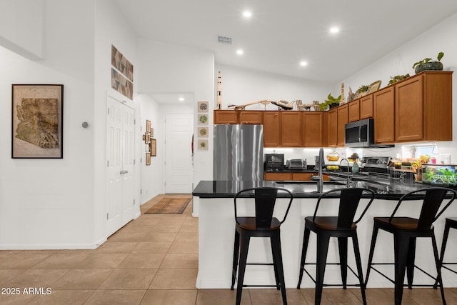 1725 E Chanute Pass, Phoenix, AZ 85040 - kitchen with stainless steel appliances, a peninsula, dark countertops, brown cabinetry, and a breakfast bar area
