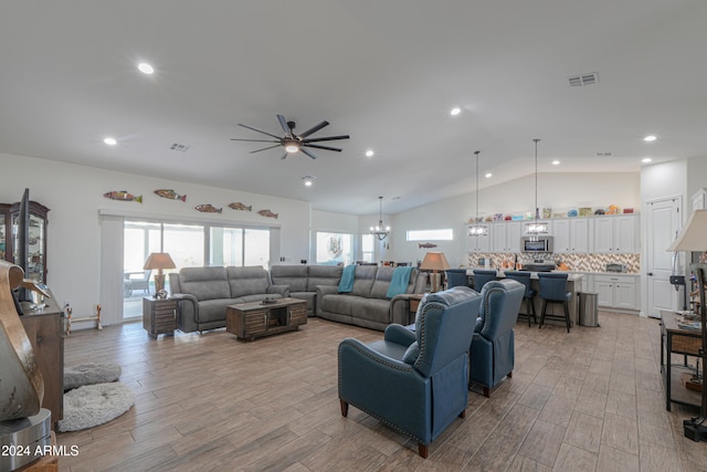 living room featuring lofted ceiling, ceiling fan with notable chandelier, and light wood-type flooring