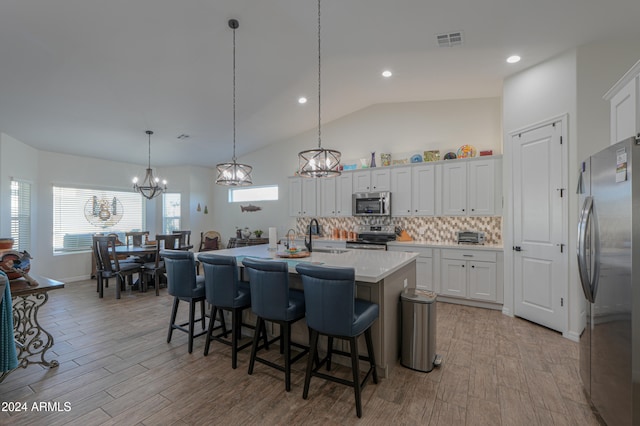 kitchen with lofted ceiling, stainless steel appliances, decorative light fixtures, white cabinets, and light hardwood / wood-style floors