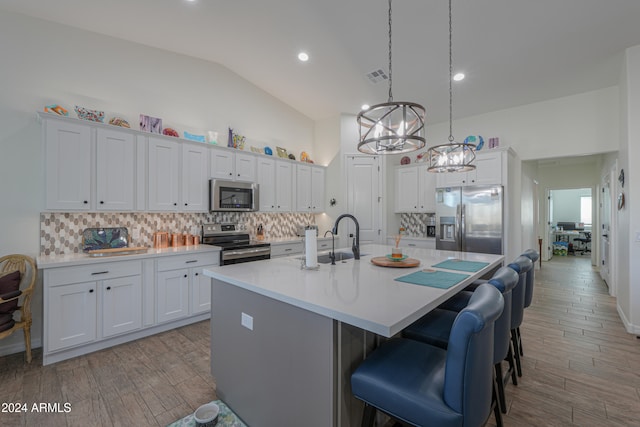 kitchen with stainless steel appliances, vaulted ceiling, pendant lighting, white cabinetry, and light hardwood / wood-style floors