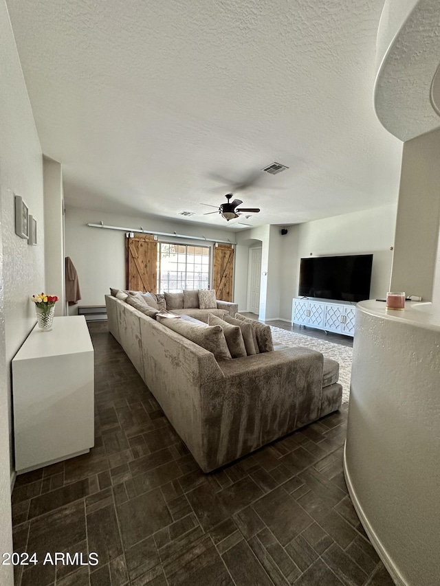 living room with dark tile floors, a barn door, ceiling fan, and a textured ceiling