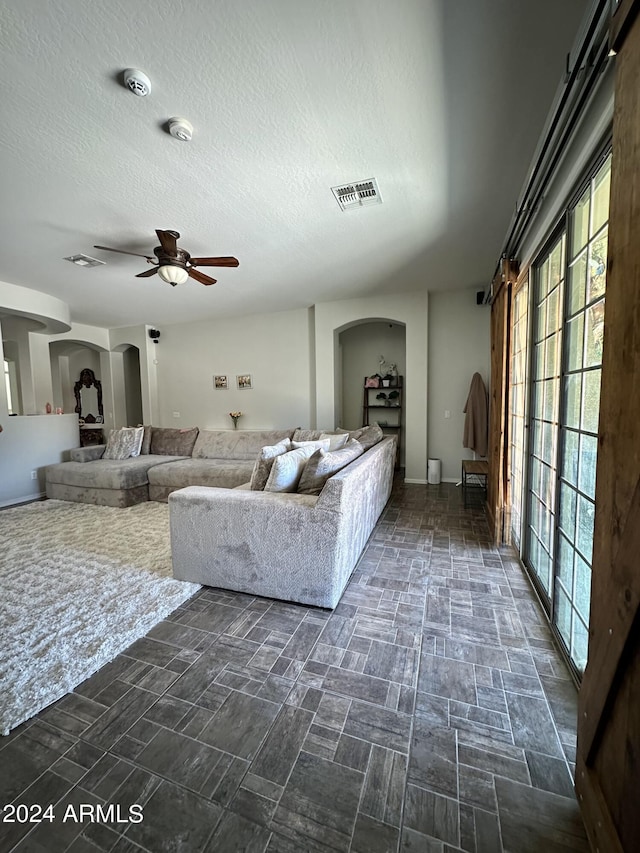 unfurnished living room with a textured ceiling, ceiling fan, and dark tile floors