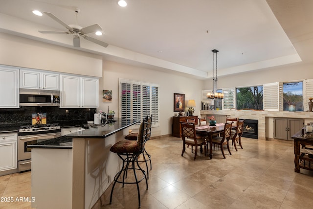 kitchen with a raised ceiling, appliances with stainless steel finishes, pendant lighting, and white cabinets