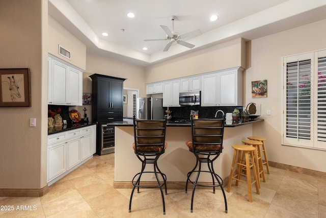 kitchen with a breakfast bar area, kitchen peninsula, a raised ceiling, stainless steel appliances, and backsplash