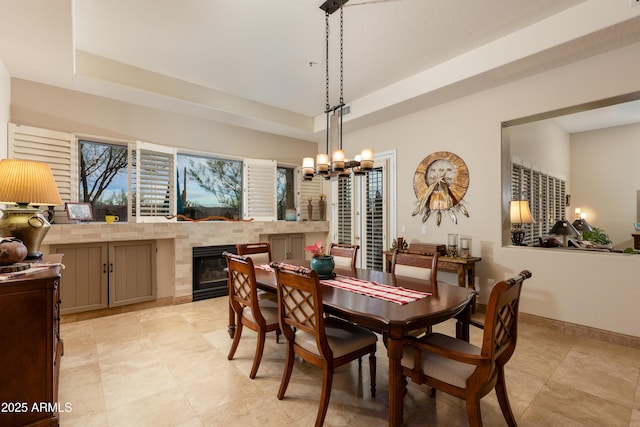 dining space featuring a raised ceiling, an inviting chandelier, and a fireplace