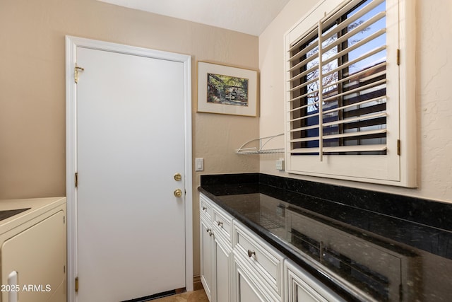 kitchen with white cabinetry, washer / dryer, and dark stone counters