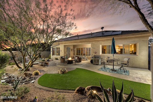 back house at dusk featuring a fire pit, a lawn, a patio area, and solar panels