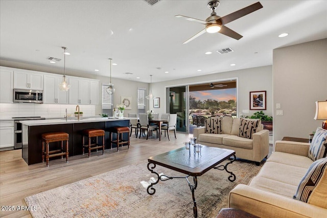 living room featuring light wood finished floors, a ceiling fan, and recessed lighting