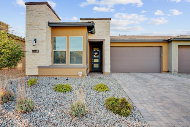 contemporary home with a garage, decorative driveway, stucco siding, and stone siding