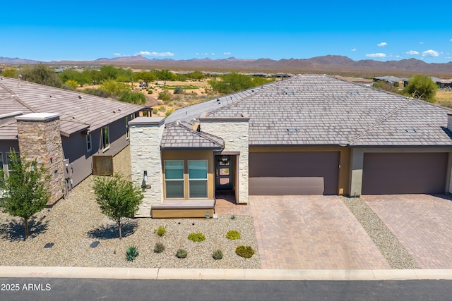 view of front of property featuring stucco siding, stone siding, a mountain view, decorative driveway, and an attached garage