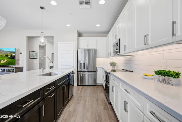 kitchen featuring appliances with stainless steel finishes, a sink, white cabinetry, decorative light fixtures, and backsplash