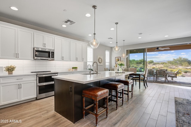 kitchen with appliances with stainless steel finishes, light wood-style flooring, a sink, a center island with sink, and recessed lighting