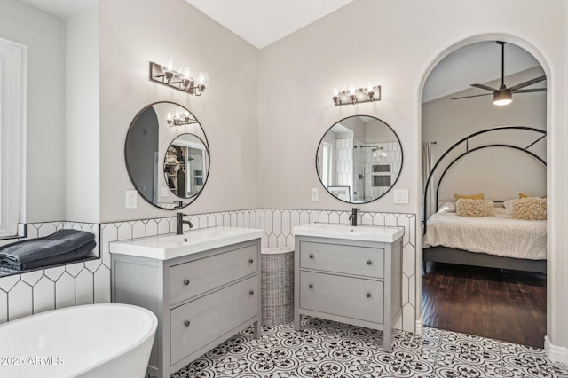 bathroom with a soaking tub, two vanities, ensuite bathroom, wainscoting, and a sink