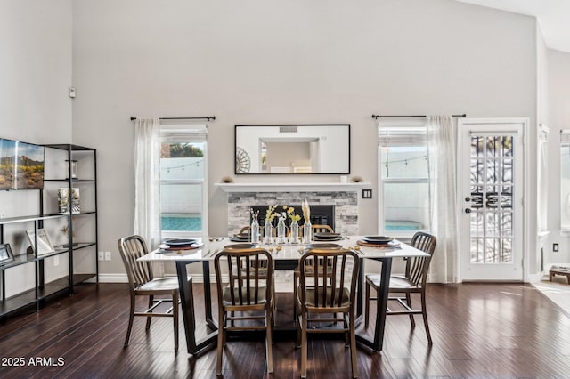 dining area featuring dark wood-type flooring, a fireplace, a high ceiling, and baseboards