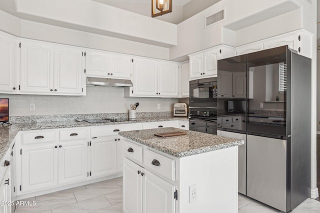 kitchen featuring a center island, light stone countertops, under cabinet range hood, black appliances, and white cabinetry