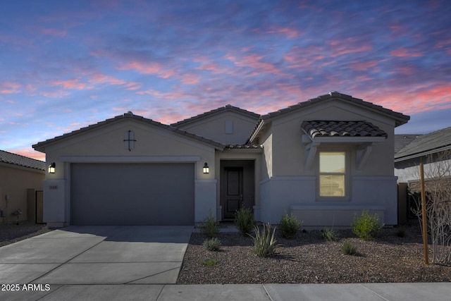 view of front of home featuring stucco siding, driveway, a tiled roof, and a garage