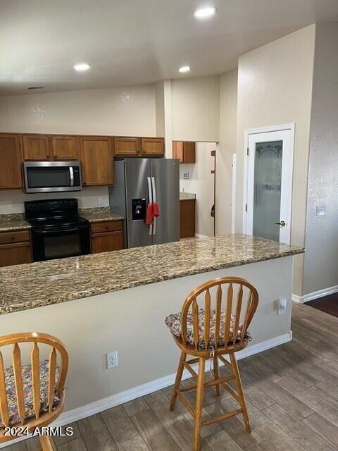 kitchen with light stone counters, appliances with stainless steel finishes, dark hardwood / wood-style floors, and vaulted ceiling