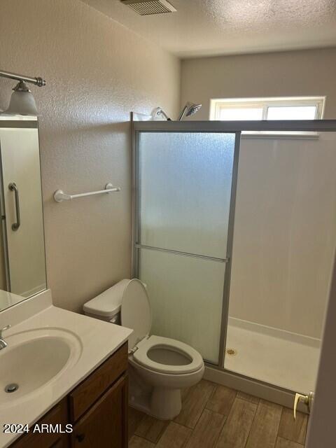 bathroom featuring vanity, wood-type flooring, a textured ceiling, walk in shower, and toilet