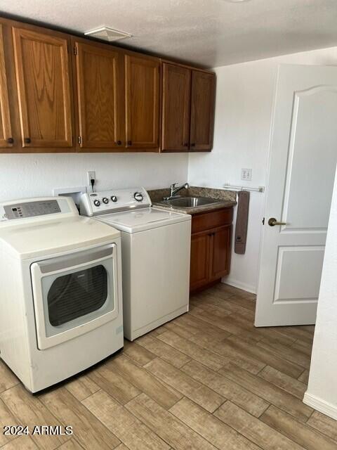 laundry area with cabinets, light wood-type flooring, washer and clothes dryer, and sink