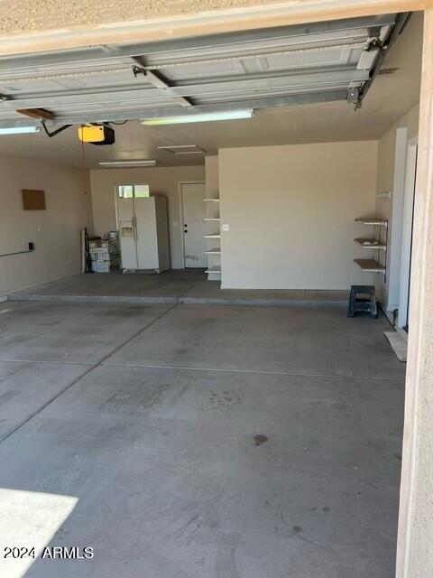 garage featuring a garage door opener and white refrigerator with ice dispenser