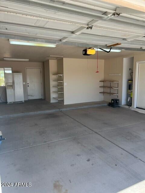 garage with a garage door opener, white refrigerator with ice dispenser, and electric water heater