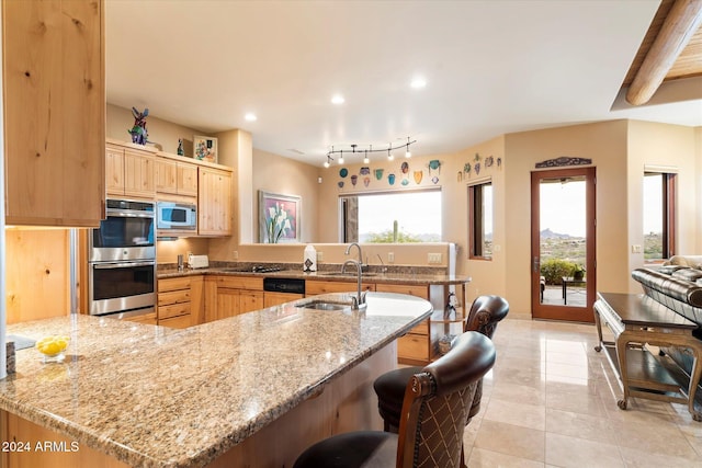 kitchen with kitchen peninsula, light brown cabinetry, white microwave, and light stone counters