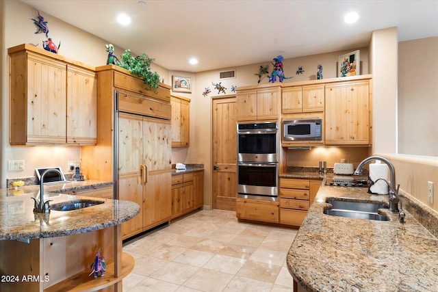 kitchen featuring light stone countertops, light brown cabinetry, built in appliances, and sink