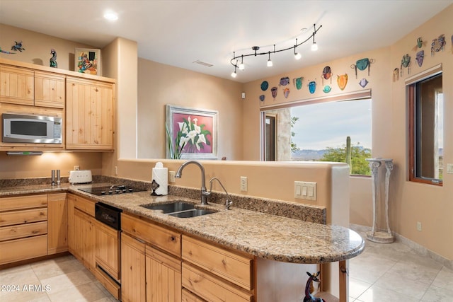 kitchen with light stone countertops, light brown cabinetry, kitchen peninsula, sink, and stainless steel microwave