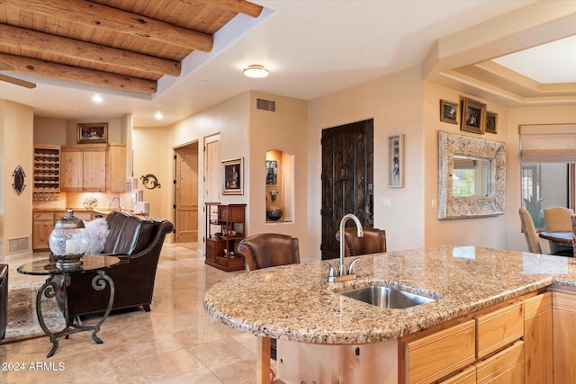 kitchen featuring beam ceiling, sink, light stone counters, light brown cabinetry, and wood ceiling