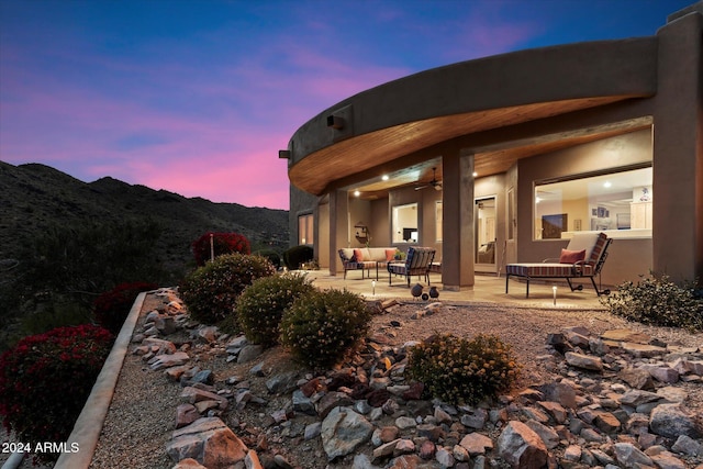 back house at dusk with an outdoor living space, a mountain view, and a patio