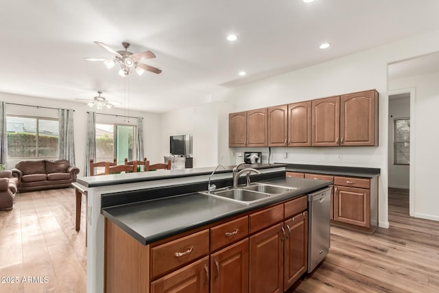 kitchen featuring a center island with sink, a sink, dishwasher, dark countertops, and open floor plan