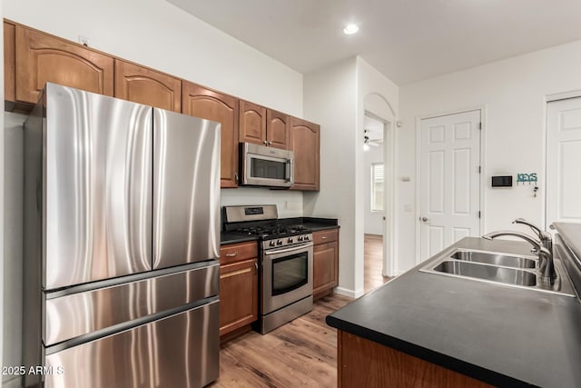 kitchen with dark countertops, wood finished floors, brown cabinetry, stainless steel appliances, and a sink