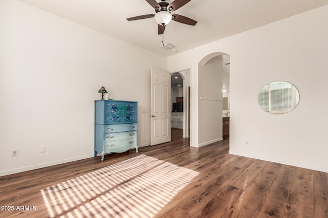 unfurnished bedroom featuring connected bathroom, baseboards, arched walkways, and wood finished floors